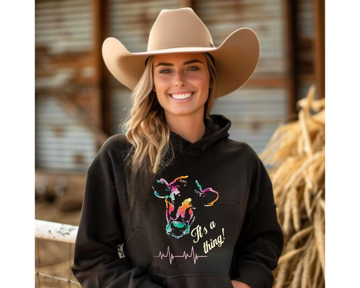 Woman wearing a black hoodie with colorful graphic and text, standing in a barn setting.