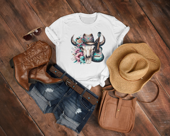 White t-shirt with a graphic design of a skull, boots, shorts, hat, and purse on a wooden surface