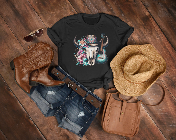 Black t-shirt with skull and guitar design, cowboy boots, hat, and purse on wooden surface