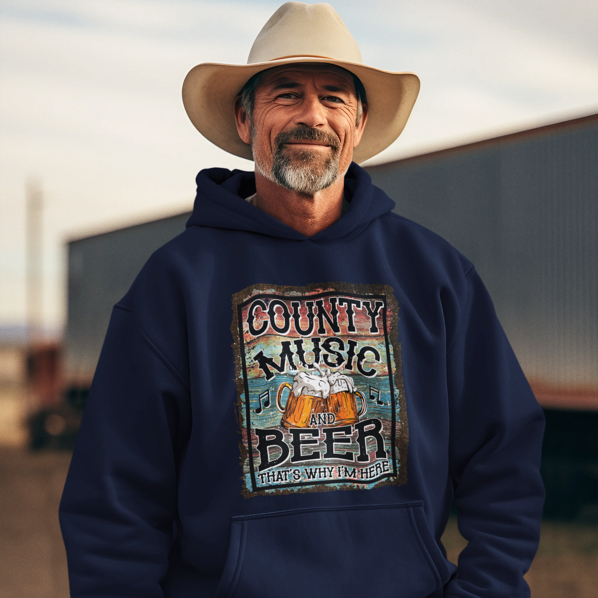Man wearing a navy hoodie with 'County Music and Beer That's Why I'm Here' design, standing outdoors.